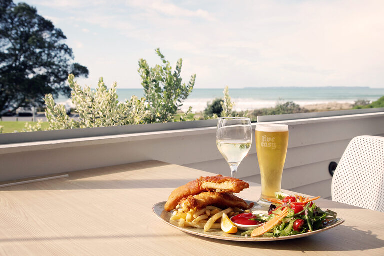 Papamoa Beach restaurant plate of food and beer overlooking the water | Tasman Holiday Parks Papamoa Beach