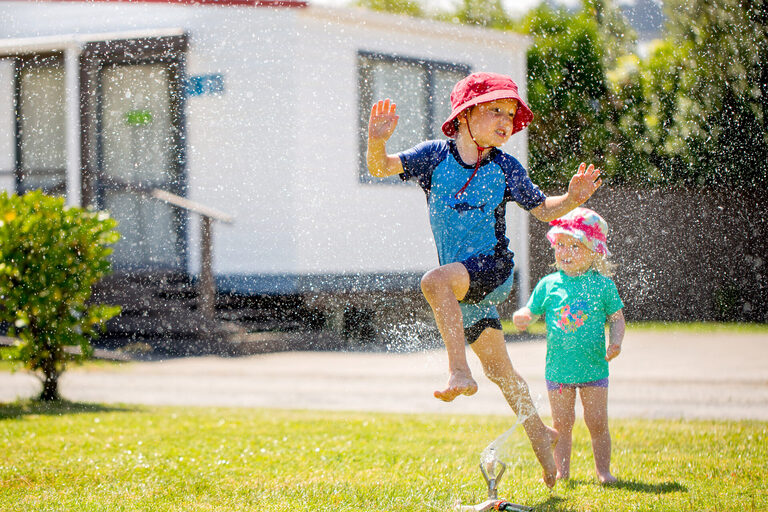 Two children running through a sprinkler | Tasman Holiday Parks
