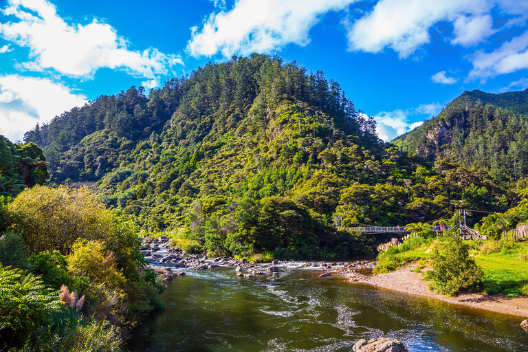The river flows among abandoned gold mines. Travel to New Zealand, North Island. Karangahake Gorge. The blue sky is reflected in the water. Tasman Holiday Parks Waihi Beach
