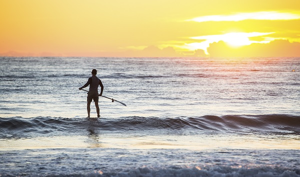 Man heading out for a morning of stand-up paddleboarding at Tathra Beach, Tathra.