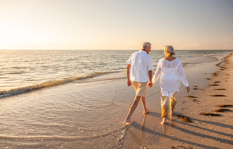 Happy senior man and woman couple walking and holding hands on a beach at sunset