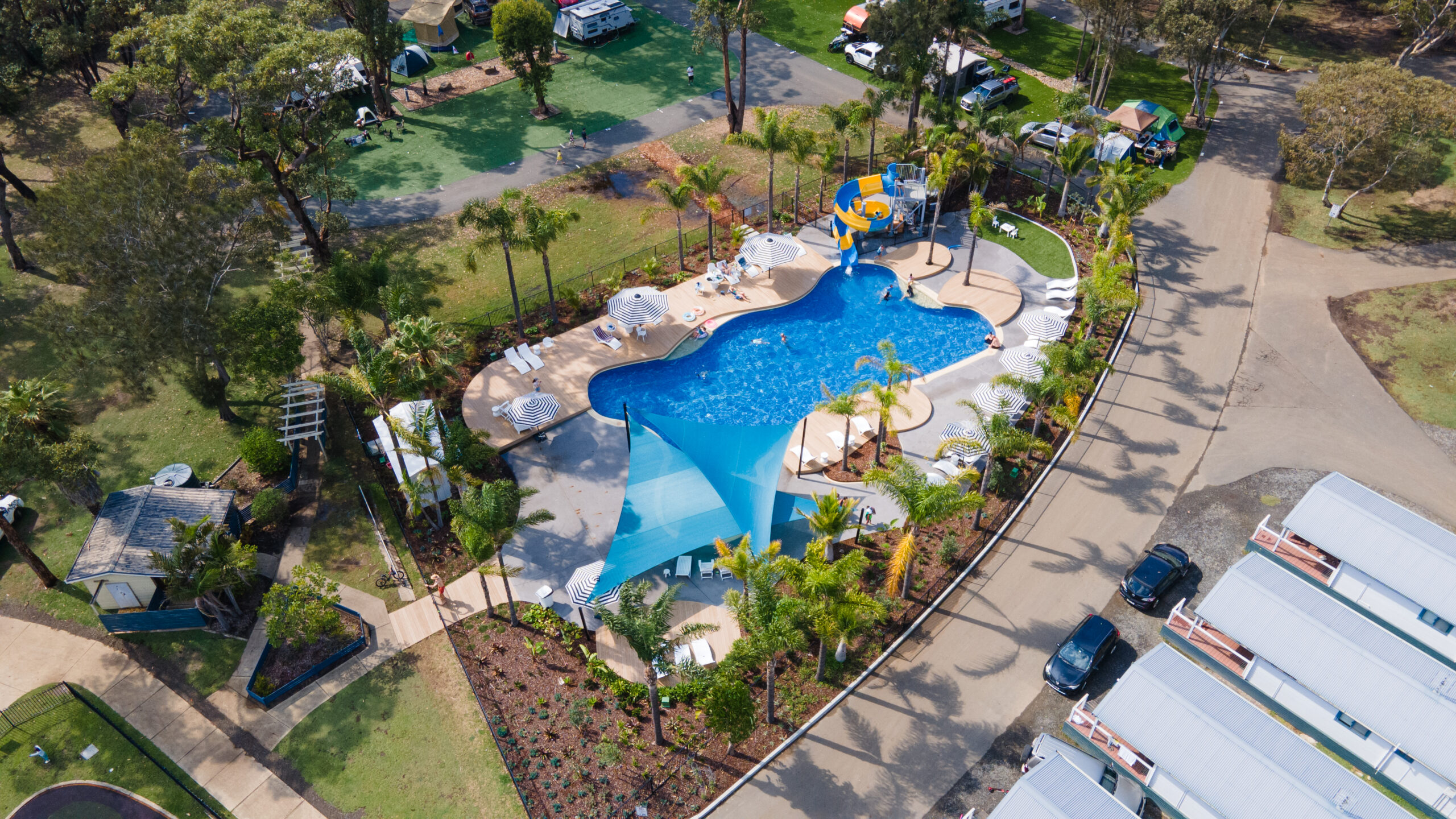 Aerial of swimming pool with surrounding cabins and caravan camping sites | Tasman Holiday Parks Racecourse Beach