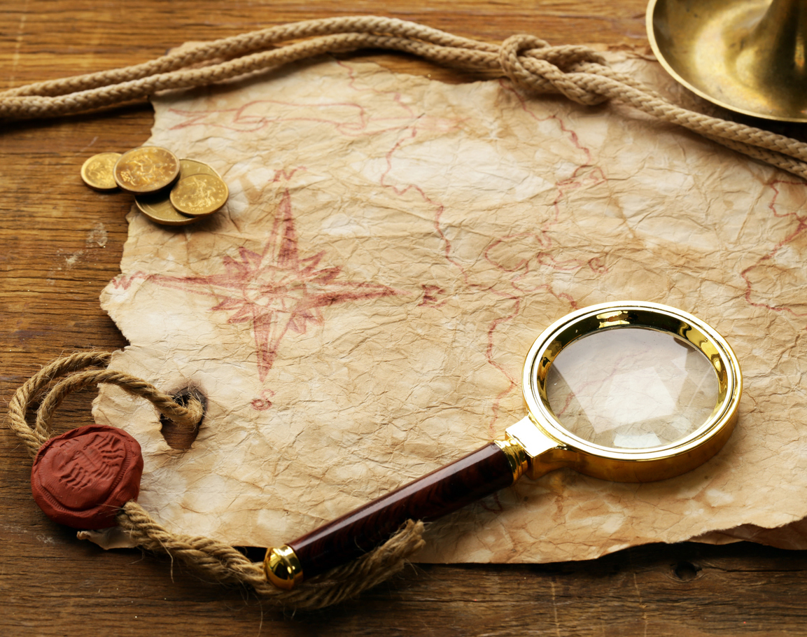 A vintage map with a red compass rose lies on a wooden surface, partially covered by a thick rope and a few gold coins. A magnifying glass with a gold rim and a wax seal attached to the rope are also on the map.