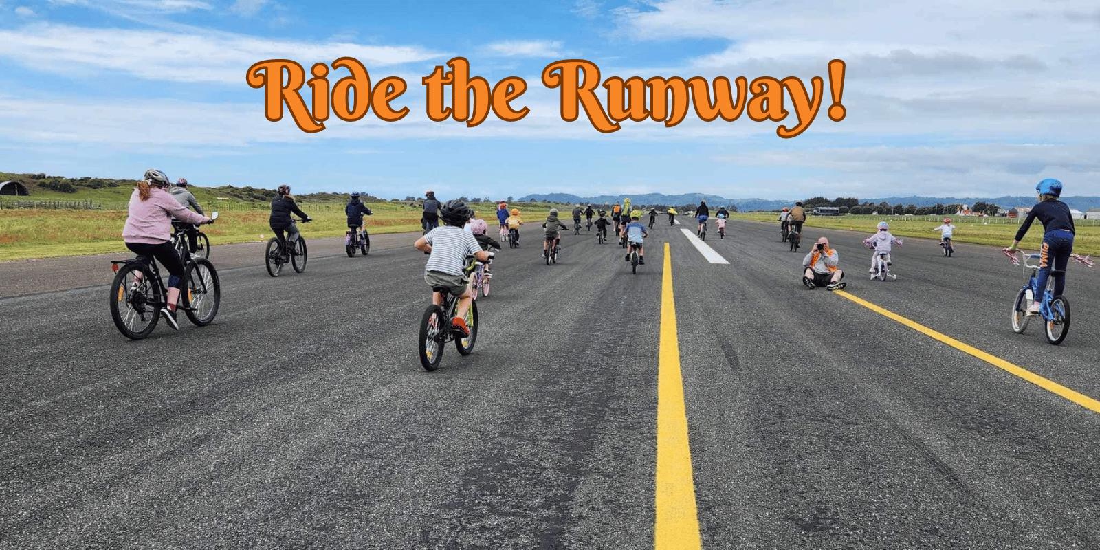 A group of people, including adults and children, ride bicycles on an open runway under a blue sky. The text "Ride the Runway!" is prominently displayed in orange and outlined in black above the participants. The atmosphere is lively and recreational.