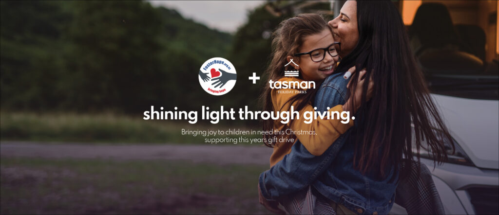 A woman and child embrace with smiles outdoors near a van. The text reads: "Shining light through giving. Bringing joy to children in need this Christmas season, supporting this year’s gift drive." Logos of two organizations are visible at the top supporting the Foster Hope and Tasman Holiday Parks Christmas Gift Drive.