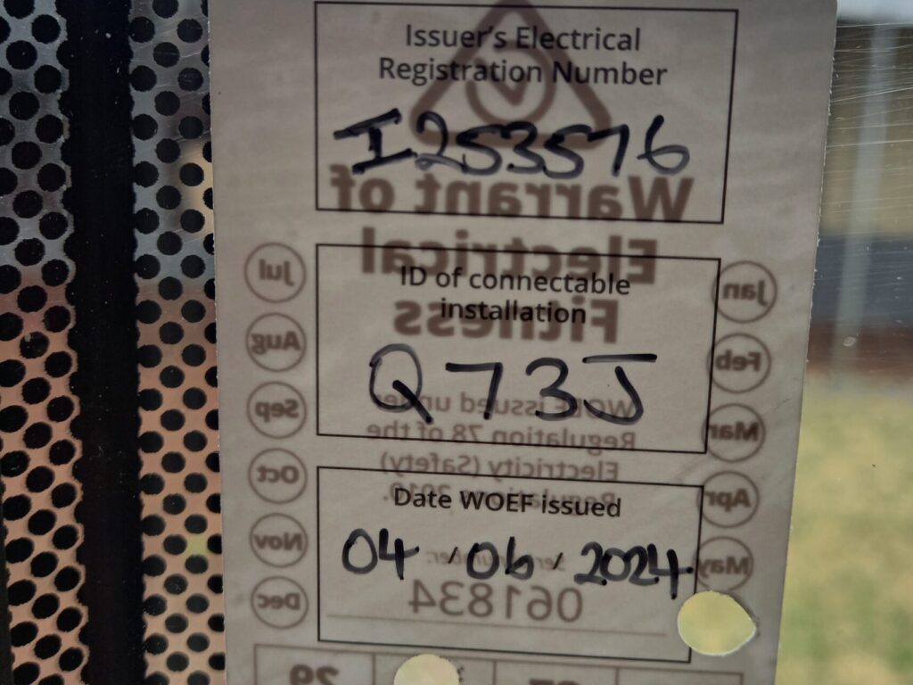 Close-up of an electrical safety label on a window. It includes registration number "1953516," date "04/06/2024," and codes "123W" and "QW2JW." The label is bordered by a dotted pattern.